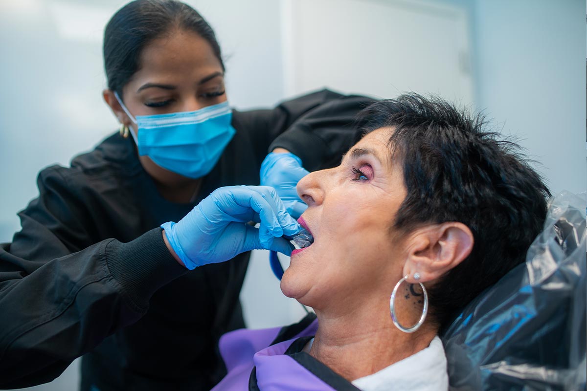 Dental assistant placing cosmetic trays into female patient's mouth